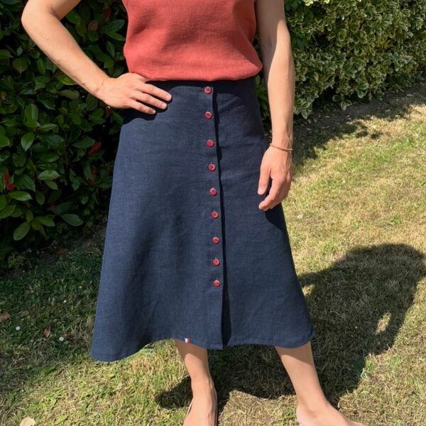 Jupe en lin bleue évasée portée sur une femme. Elle est fermée par 10 boutons rouges sur tout le devant.