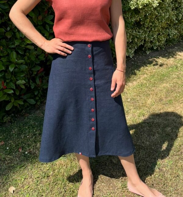 Jupe en lin bleue évasée portée sur une femme. Elle est fermée par 10 boutons rouges sur tout le devant.