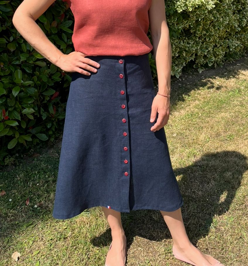Jupe en lin bleue évasée portée sur une femme. Elle est fermée par 10 boutons rouges sur tout le devant.