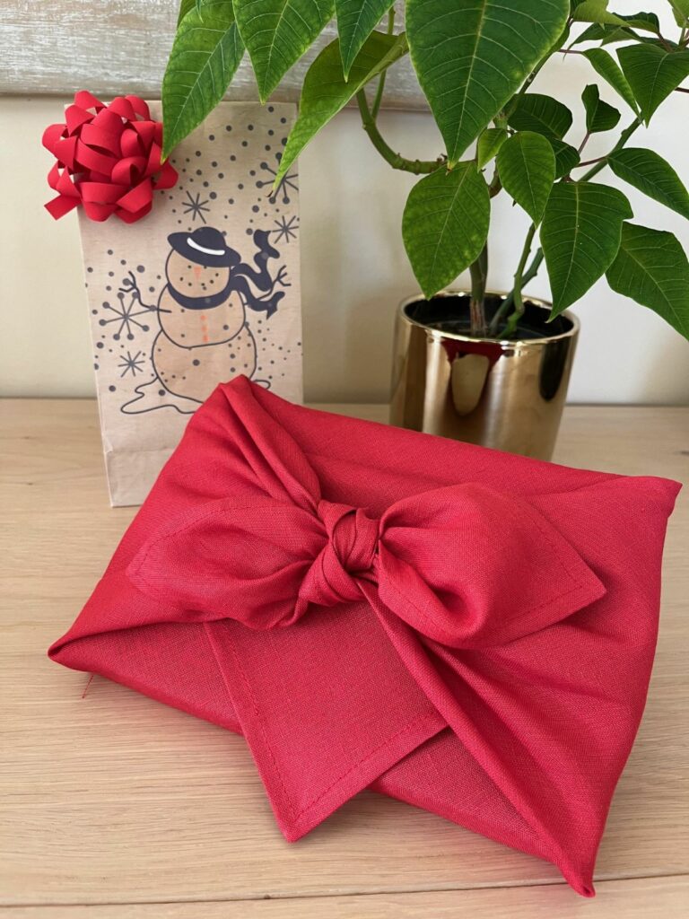 Emballage cadeau mis en scène pour Noël à côté d'une plante et d'un paquet cadeau.